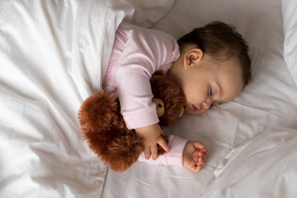 本物の肖像画かわいい白いベッドの上でテディベアとピンクの睡眠中のかわいい白人の小さな赤ちゃんぽっちゃりの女の子や男の子。お昼休みの子。ケア、睡眠の子供、子供、親、人生の概念 - 写真・画像