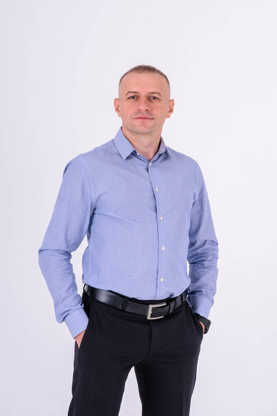 A man in a blue shirt and black trousers stands on a white background - Φωτογραφία, εικόνα