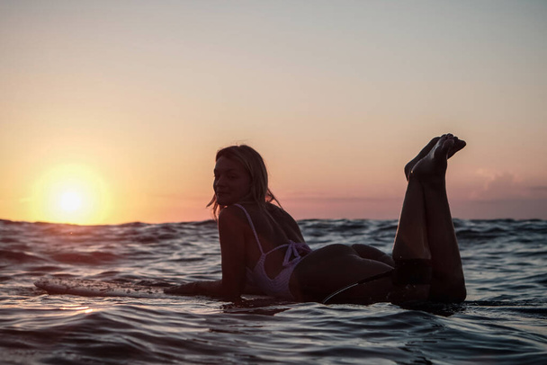 Portrait from the water of surfer girl with beautiful body on surfboard in the ocean at sunset time in Bali - Foto, Bild