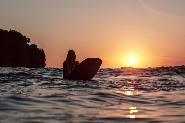 Portrait from the water of surfer girl with beautiful body on surfboard in the ocean at sunset time in Bali - 写真・画像