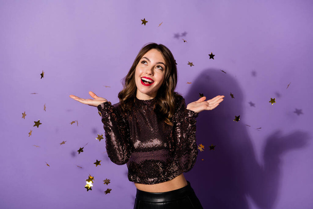 Portrait of charming cheerful girl having fun sequins flying festal day isolated over bright violet color background - Foto, Imagen