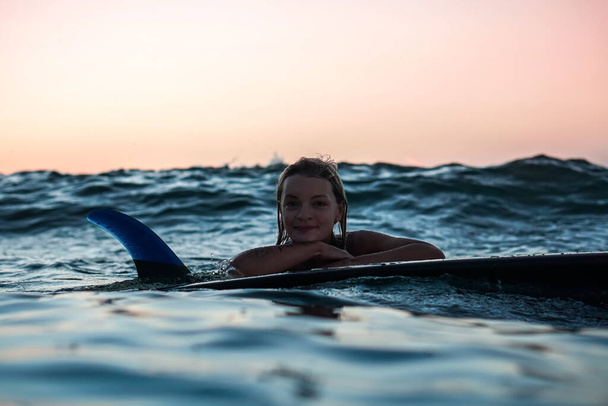 Portrait from the water of surfer girl with beautiful body on surfboard in the ocean at sunset time in Bali - Photo, image