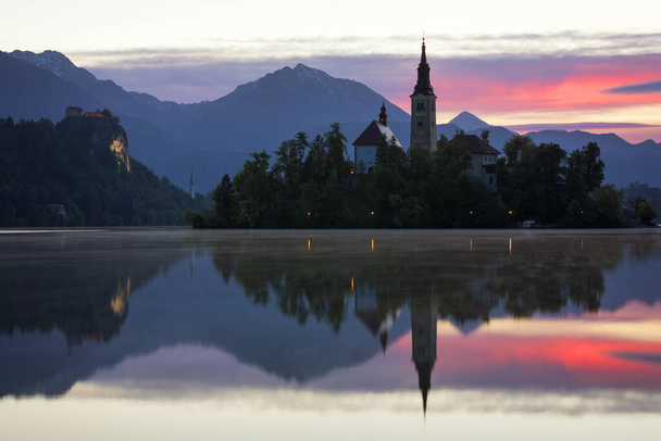 Δραματική ανατολή στη λίμνη Bled, θέα στην ανατολή Bled λίμνη, νησί, Προσκύνημα Εκκλησία της Κοιμήσεως της Θεοτόκου της Μαρίας και του Κάστρου με οροσειρά (Stol, Vrtaca, Begunjscica). Bled, Σλοβενία, - Φωτογραφία, εικόνα