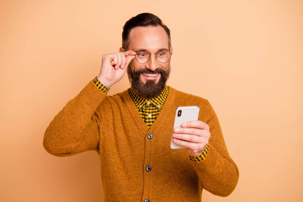 Portrait of astonished positive guy hand touch glasses look phone isolated on beige color background - Foto, afbeelding