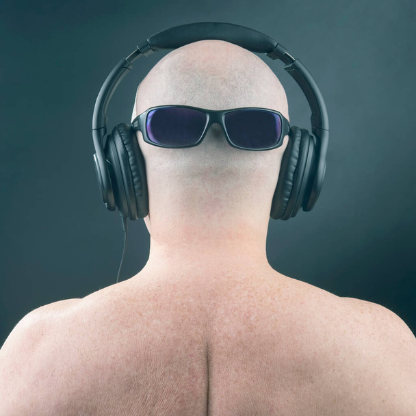 Голый мужчина слушает музыку в наушниках и солнцезащитных очках на затылке на тёмном фоне - Фото, изображение