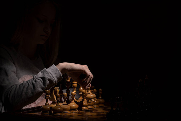 meisje in de schaduw speelt vintage schaken op een donkere achtergrond. Oud schaken. bedrijfsconcept. - Foto, afbeelding