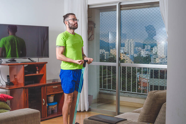 Ritratto di giovane uomo che usa camicia verde e pantaloncini blu per allenarsi a casa - Foto, immagini