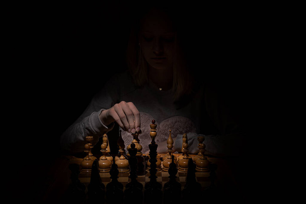 girl in the shadows plays vintage chess on a dark background. old chess. business concept. - Foto, afbeelding