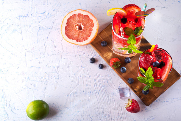 cocktail with mint, strawberry and orange on a wooden stand on a white table with space for text - Fotoğraf, Görsel