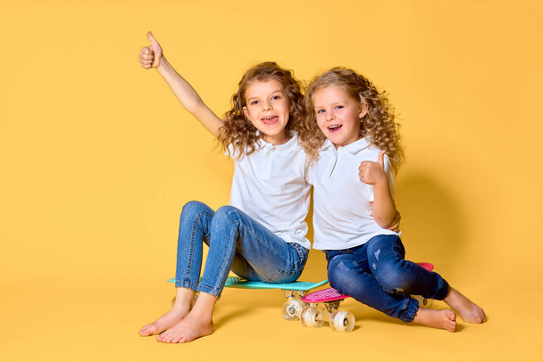 Two Active and happy girls with curly hair having fun with penny - 写真・画像