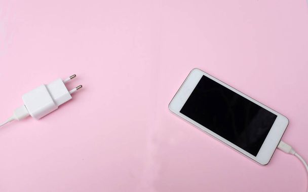 πάνω όψη και επίπεδη θέσει λευκό Smartphone Plug In με φορτιστή προσαρμογέα σε ροζ παστέλ φόντο - Φωτογραφία, εικόνα