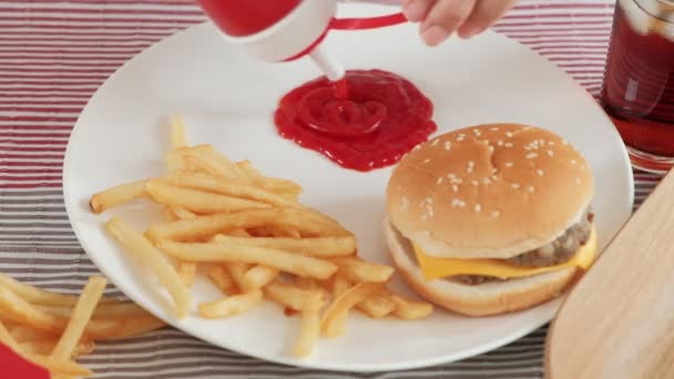 Close-ups, enfoque selectivo en ketchup en un plato blanco en manteles que se vierten de botellas rojas para aperitivos de comida chatarra, incluyendo hamburguesas para llevar, papas fritas, bocadillos y cola.  - Metraje, vídeo