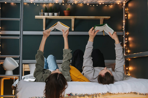 Funny couple reading books in bed, holding them in outstreched arms. Both lying on their backs. - Fotó, kép