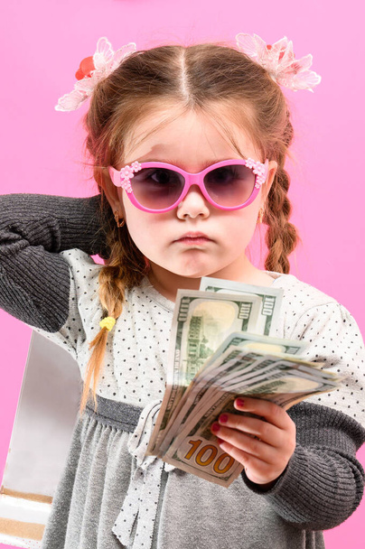 Dziewczynka w okularach z paczką i pieniędzmi na różowym tle, dziecko i zakupy. nowe - Zdjęcie, obraz