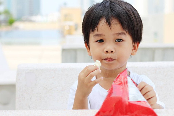 asiatico ragazzo seduta su un cemento sedia e mangiare un snack. - Foto, immagini