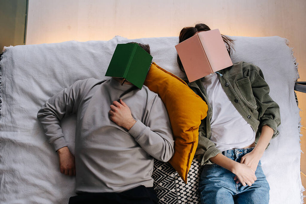 Cute funny couple napping with face covered with a book. Top view. Wearing casual daily clothes. - Fotó, kép