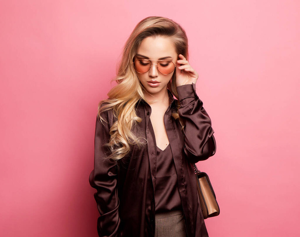 Beautiful blond woman in a blouse and pants wearing glasses, holding handbag - Foto, afbeelding