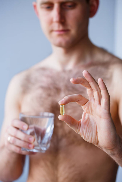 Un joven tiene vitaminas y un vaso de agua en sus manos. Píldoras de inmunidad - Foto, Imagen