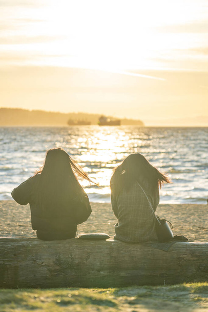 Dos niñas disfrutan de la puesta de sol en English Bay Beach, Vancouver City hermoso paisaje. Concepto de ocio adolescente. - Foto, imagen
