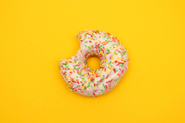 Donut with colorful sprinkles on yellow background. Pink frosted donut with colorful sprinkles - Photo, Image