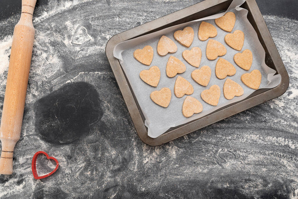 Домашняя выпечка. Деревянная скалка и лист для выпечки с печеньем в форме сердца - Фото, изображение