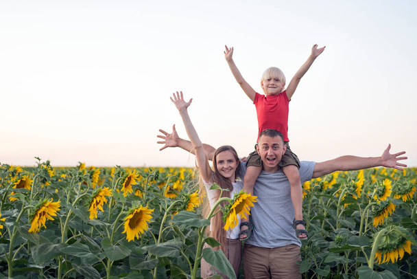 Young family stands on field of sunflowers with their hands up. Happy family. Rural vacation. - Foto, Bild