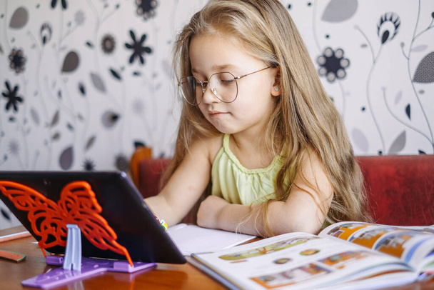 Distance learning. Home online learning. Little girl teaches English, speaks with a teacher online. - Photo, Image