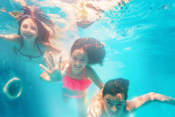 Group of three friends children dive underwater together waving hands and smiling - Foto, imagen