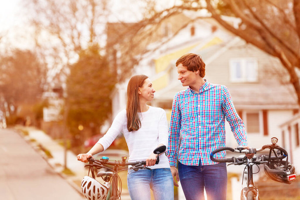 Beautiful young couple walk with bicycles outside on typical American urban street - Valokuva, kuva