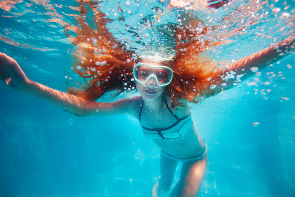 Beautiful underwater portrait of the smiling little girl with long hairs wearing scuba mask in the pool - Valokuva, kuva