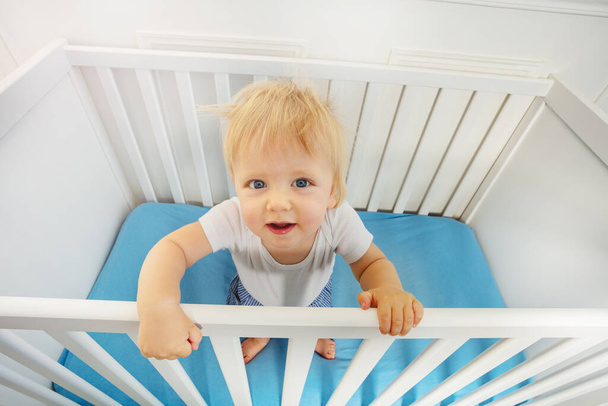 Portrait of cute little blond toddler boy in in the baby crib looking up - Fotoğraf, Görsel
