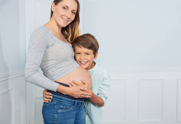 Pregnant mother on ninth month and son hug big belly both smiling - Foto, Imagen