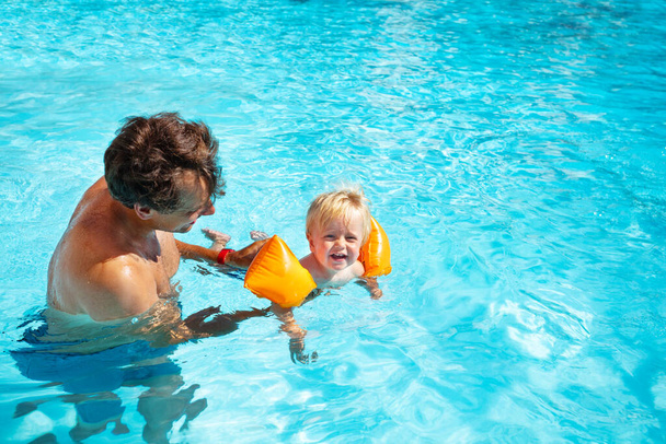 Father teaches toddler to swim in the pool wearing inflatable shoulder straps  - Zdjęcie, obraz