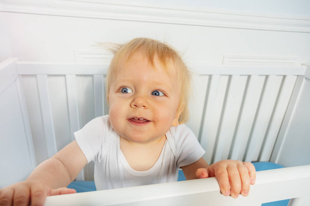 Cute laughing baby boy stand in the crib with positive expression - Photo, Image
