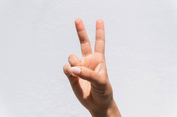 A closeup of peace hand sign against a white wall background - Fotó, kép