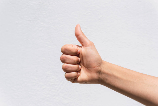 A closeup of thumbs-up hand sign against a white wall background - Fotoğraf, Görsel