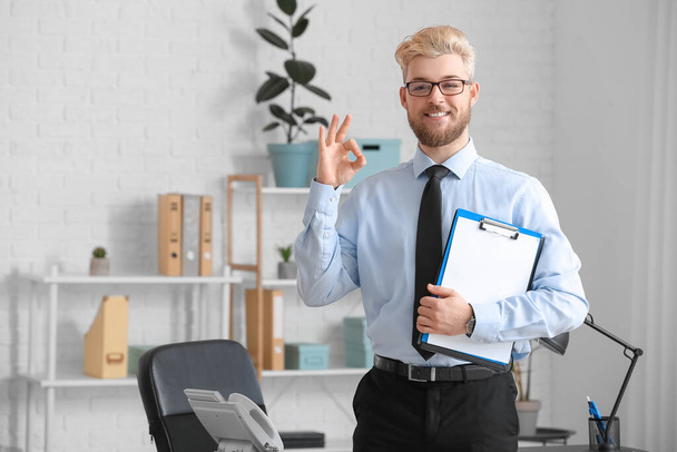 Young man with clipboard showing OK in office - Photo, Image