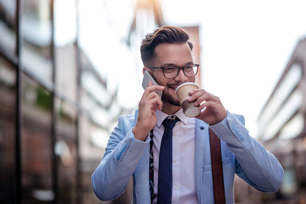 A fiatal üzletember szünetet tart, kávét iszik és mobiltelefont használ.. - Fotó, kép