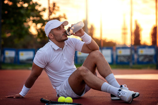 スポーツテニスの選手はテニスコートで休んでいる。フィットネスと健康的なライフスタイルの概念. - 写真・画像