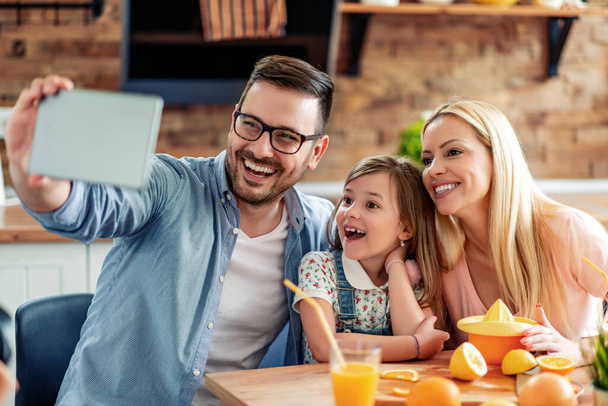 Mladá rodina se selfie při výrobě pomerančové šťávy v kuchyni. - Fotografie, Obrázek