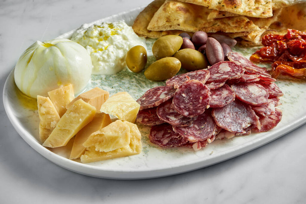 Italian antipasti snacks on white plate on marble background. Focaccia, burrata, olives, sun-dried tomatoes, salami, cheese, parmesan. - Fotografie, Obrázek