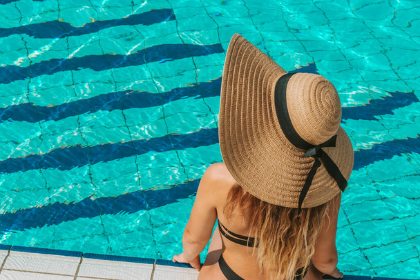 Femme par piscine. Joyeux jeune fille sexy en maillot de bain bikini, lunettes de soleil et chapeau de paille en eau bleue. Voyage de luxe style de vie - Photo, image