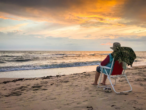 Starší žena sedící na skládacím křesle na pláži Palanga si užívá sledování západu slunce a moře v klidném večeru. Lithaunia letní dovolená. - Fotografie, Obrázek