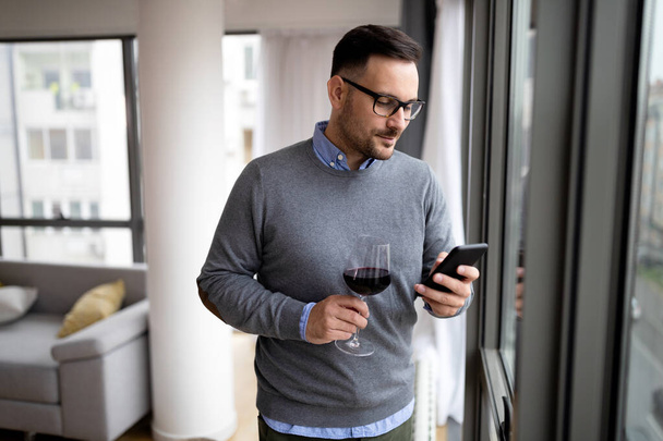 Portrait of handsome young man holding glass of red wine at home - Photo, image