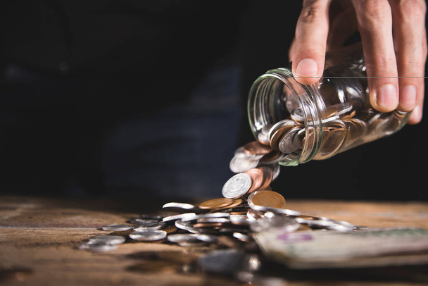 a man spills coins from a glass jar on a wooden table - Fotografie, Obrázek
