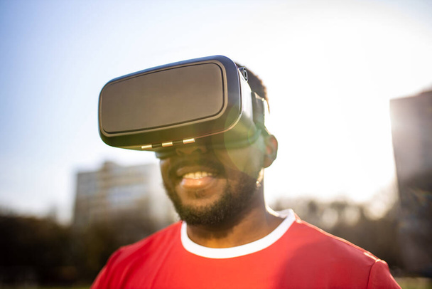 happy man in virtual reality glasses in football field background is blurred concept of virtual reality outdoors summer sunny day - Foto, imagen