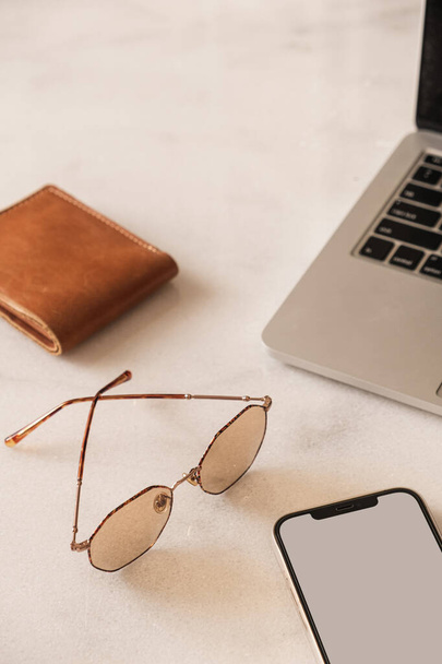 Mobile phone, laptop, wallet, glasses on marble table. Home office desk workspace. Lady, girl boss aesthetic business, work concept. Flat lay, top view - Photo, Image
