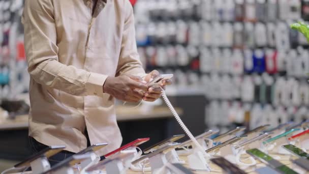 comprador masculino con máscara está eligiendo el teléfono móvil en la tienda, ver la muestra de exposición en la tienda de equipos digitales - Imágenes, Vídeo