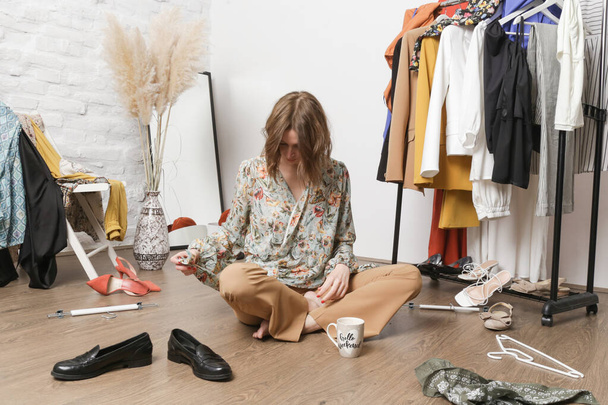 Mujer joven estresada sentada en la habitación desordenada llena de ropa. Nada que llevar concepto. - Foto, Imagen