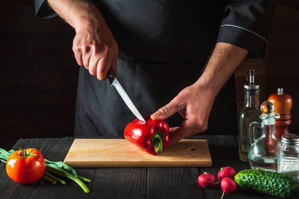 Professional chef or cook is cutting red peppers for salad on a restaurant kitchen table. Vegetable diet or snack idea. - Foto, afbeelding